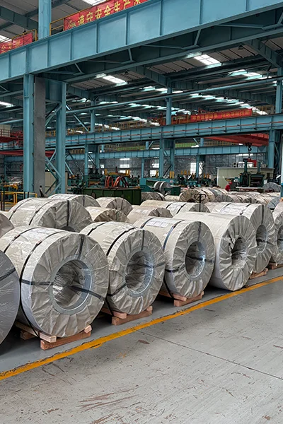An industrial exhibition display featuring massive rolls of shiny metallic CRGO (Cold Rolled Grain Oriented) electrical steel coils inside a modern manufacturing factory showroom.