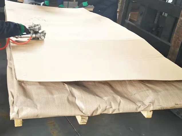 Workers applying moisture-proof wrapping and protective paper on electrical steel coil for export packaging