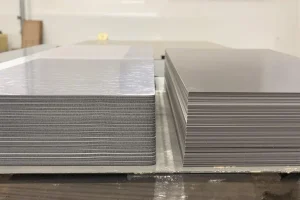 Two stacks of laminated steel sheet material side by side on a workbench, one lighter and one darker, for material comparison