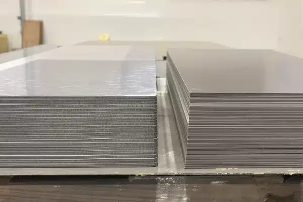 Two stacks of laminated steel sheet material side by side on a workbench, one lighter and one darker, for material comparison