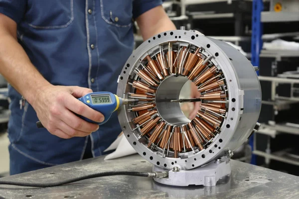 Technician measuring a motor stator core with a handheld digital gauge on a workbench