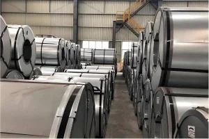 Rows of electrical steel coils stacked in a warehouse, lit from the side