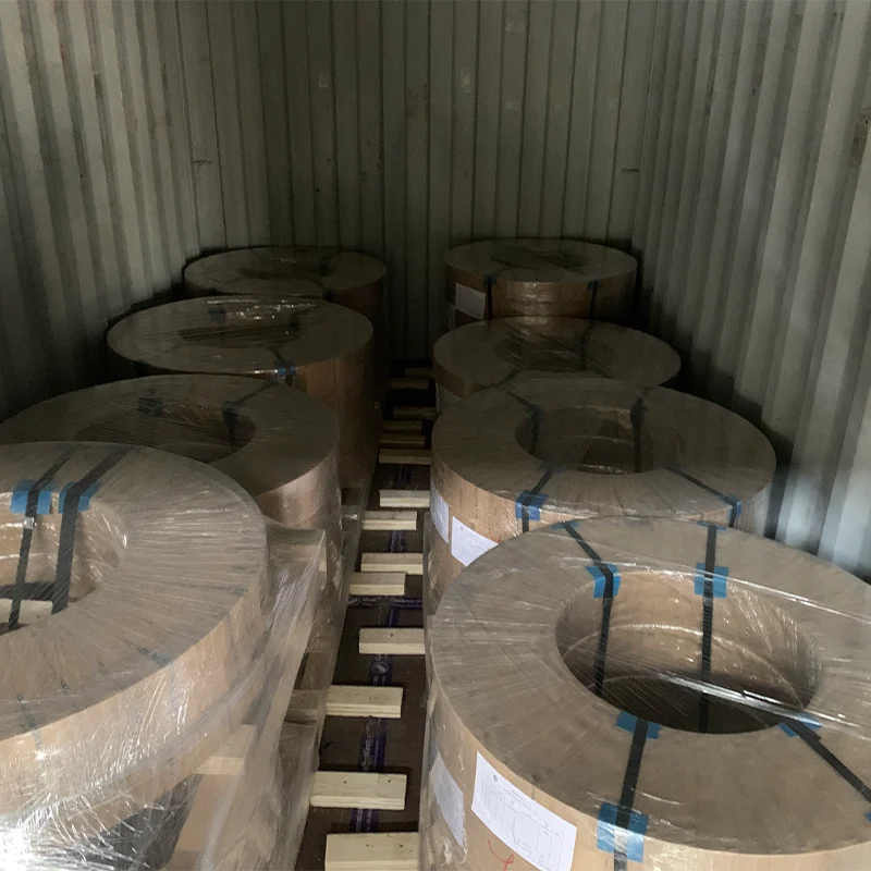 Interior of a shipping container packed with multiple wax-paper and plastic-wrapped electrical steel coils braced with wooden dunnage 