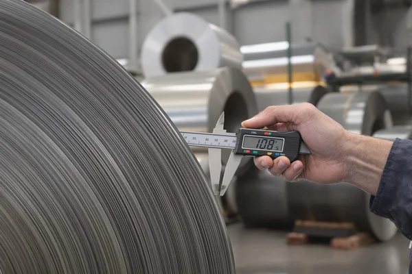 Worker using a digital caliper to measure the gauge thickness at the edge of a stacked silicon steel coil