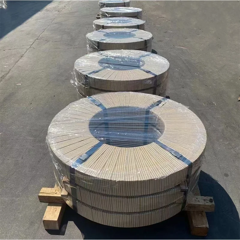 Row of narrow slit CRGO coils staged outdoors on wooden pallets in direct sunlight, wrapped in plastic and kraft paper