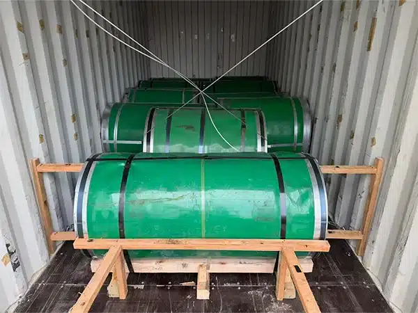 Interior of a 20ft shipping container loaded with green-wrapped CRGO electrical steel coils standing on end, braced with wooden cradle dunnage
