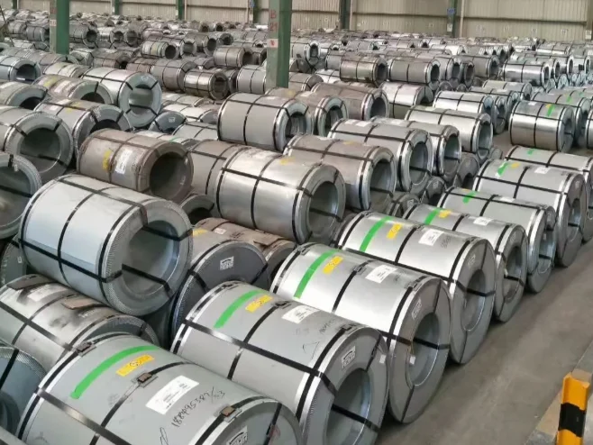 Warehouse rows of wide grain-oriented electrical steel master coils under a green structural roof frame with an overhead crane