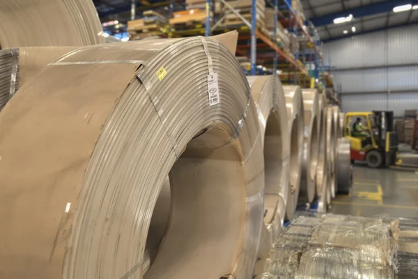 Wrapped coils of grain-oriented electrical steel on racking in a distribution warehouse with a forklift behind