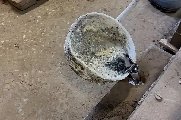 Molten aluminum poured from a ladle, showing its silvery appearance without a bright glow
