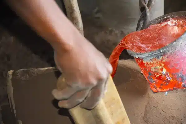 Molten aluminum being poured from a crucible into a sand mold at a small foundry