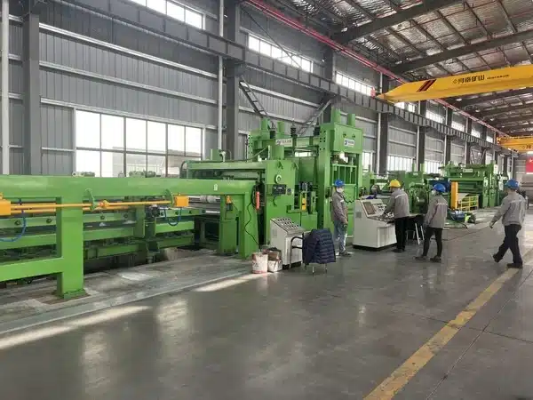 Workers monitoring a precision cold-strip slitting and processing line inside a steel mill