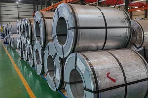 Two grain-oriented electrical steel coils side by side, one with a clean bright mill edge and one with a darker oiled and edge-damaged surface