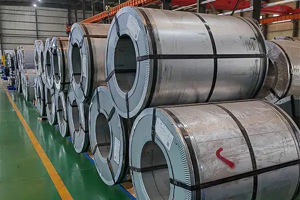 Two grain-oriented electrical steel coils side by side, one with a clean bright mill edge and one with a darker oiled and edge-damaged surface