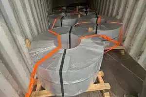 Six slit coils of 0.10mm ultra-thin grain-oriented electrical steel laid eye-to-sky on wooden pallets inside a shipping container, secured with orange ratchet straps