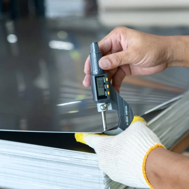 A hand using a digital micrometer to measure the thickness of a stack of thin grain-oriented electrical steel sheets