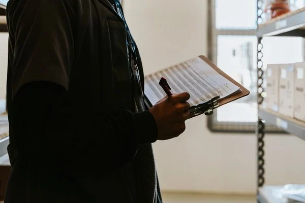 Warehouse worker checking a printed checklist against shelved inventory