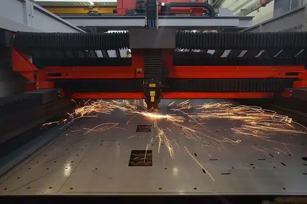 Laser cutting machine cutting a steel sheet, with sparks spraying from the cutting head across the bed