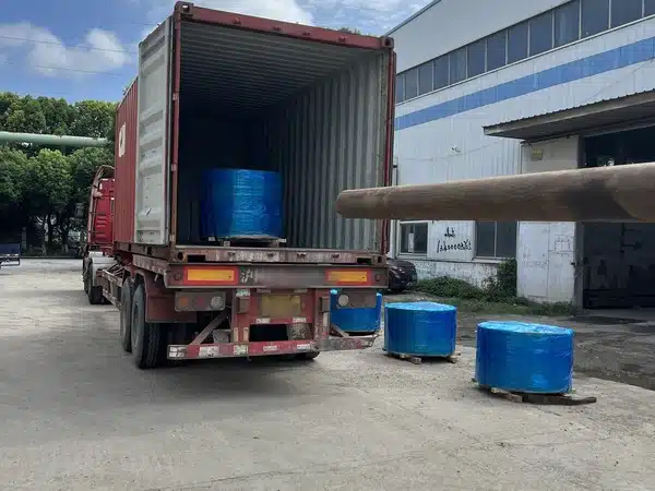 Blau umwickelte Spulen aus geschliffenem Siliziumstahlband auf Holzpaletten neben einem Containerlastwagen