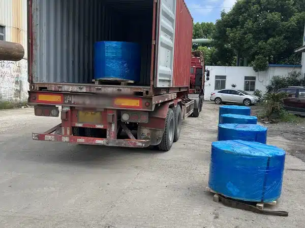 Fünf umwickelte Spulen aus geschliffenem Siliziumstahlband auf Holzpaletten, eine bereits im Container