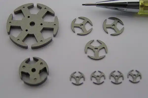 Small stamped motor laminations, some loose and some stacked into short cores, with a pencil tip for scale