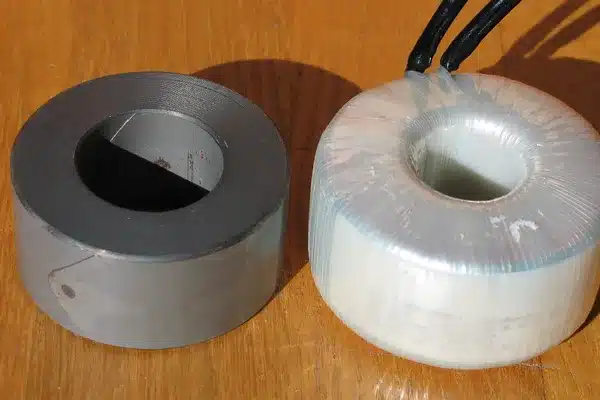 Blanker gewickelter Stahltoroidkern neben einem fertigen, mit Klebeband versehenen Toroidtransformator auf einem Holztisch